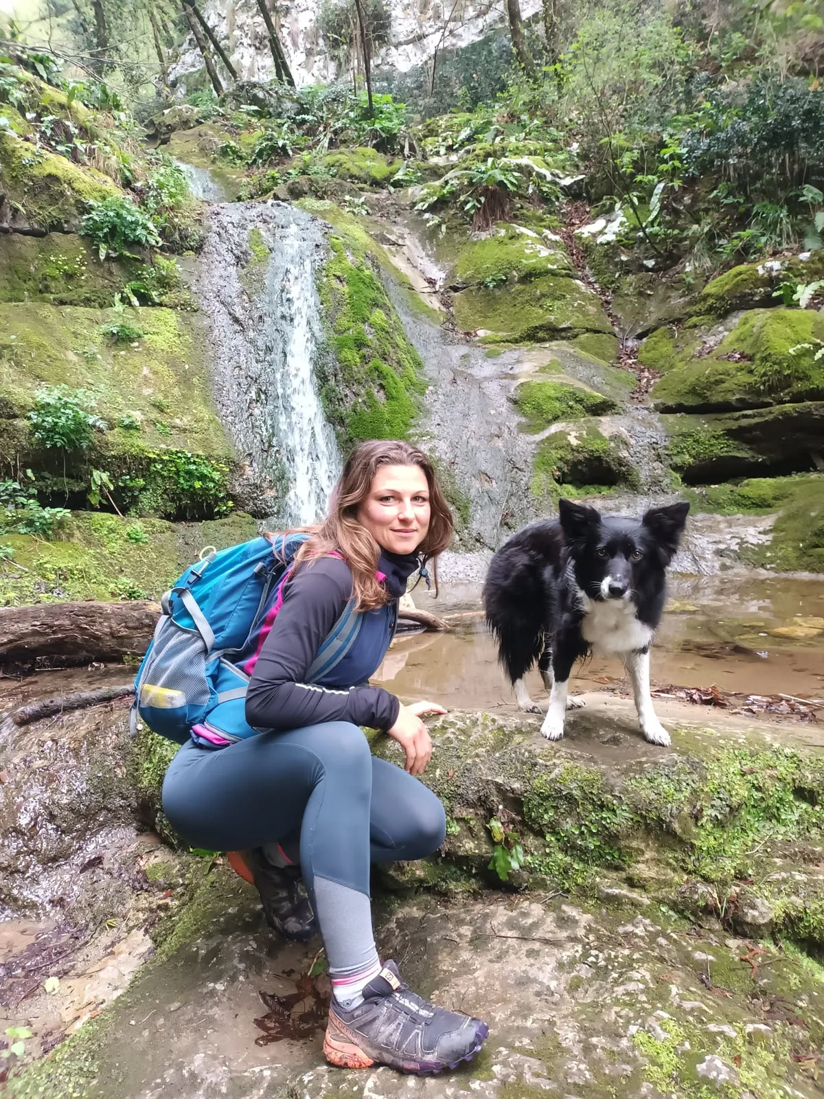 Accovacciata su una roccia vicino a una cascata, con lo zaino e il cane