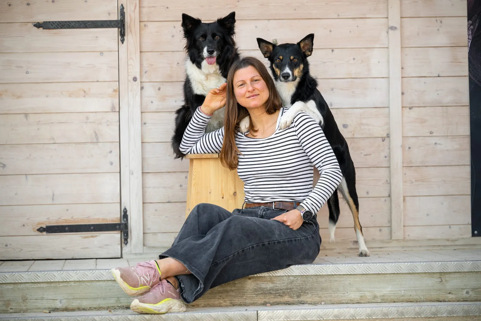 Zena Campedelli seduta davanti a una porta di legno, con i suoi due border collie