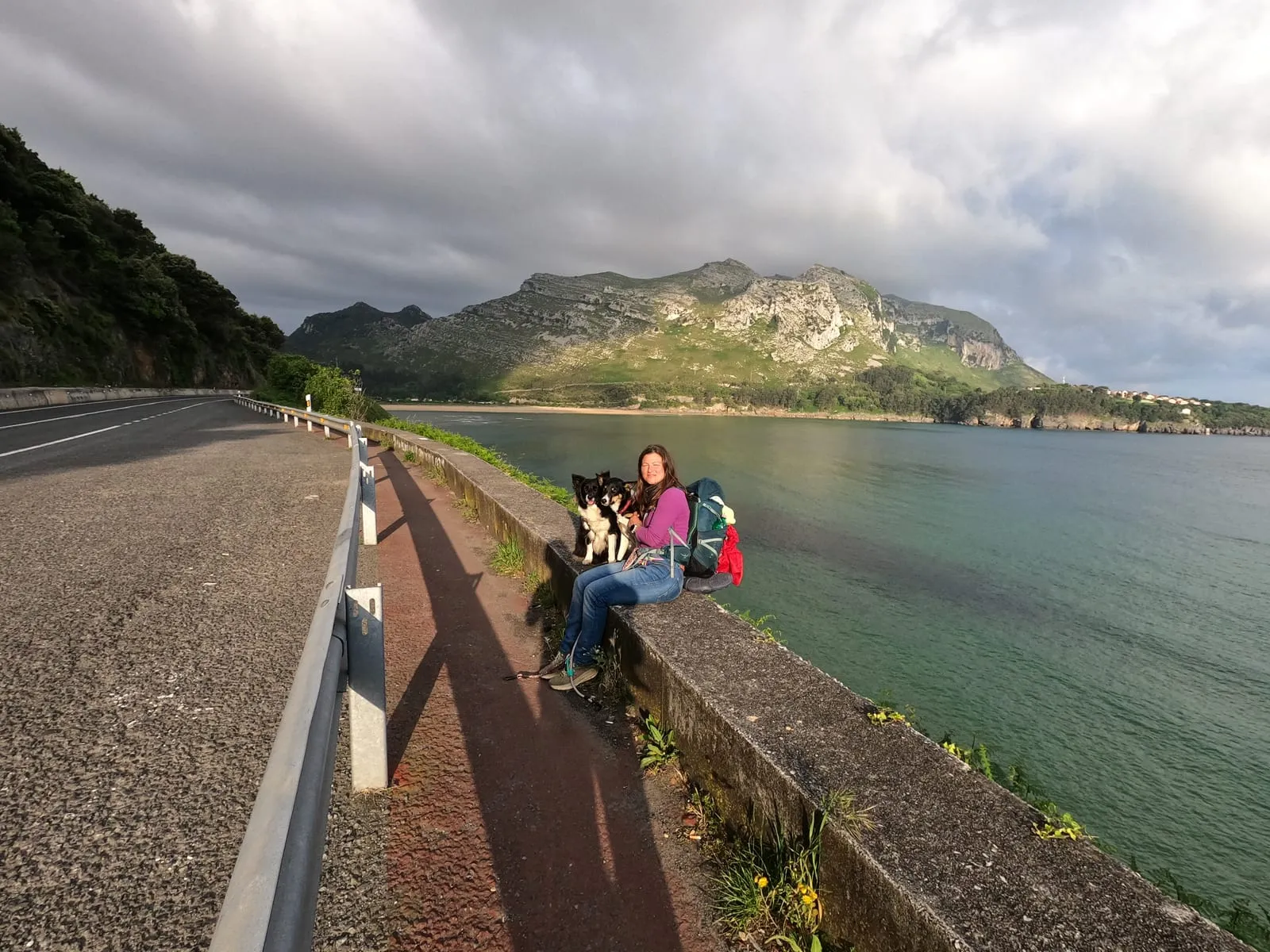 Seduta su un muretto in riva al mare, con lo zaino e i cani